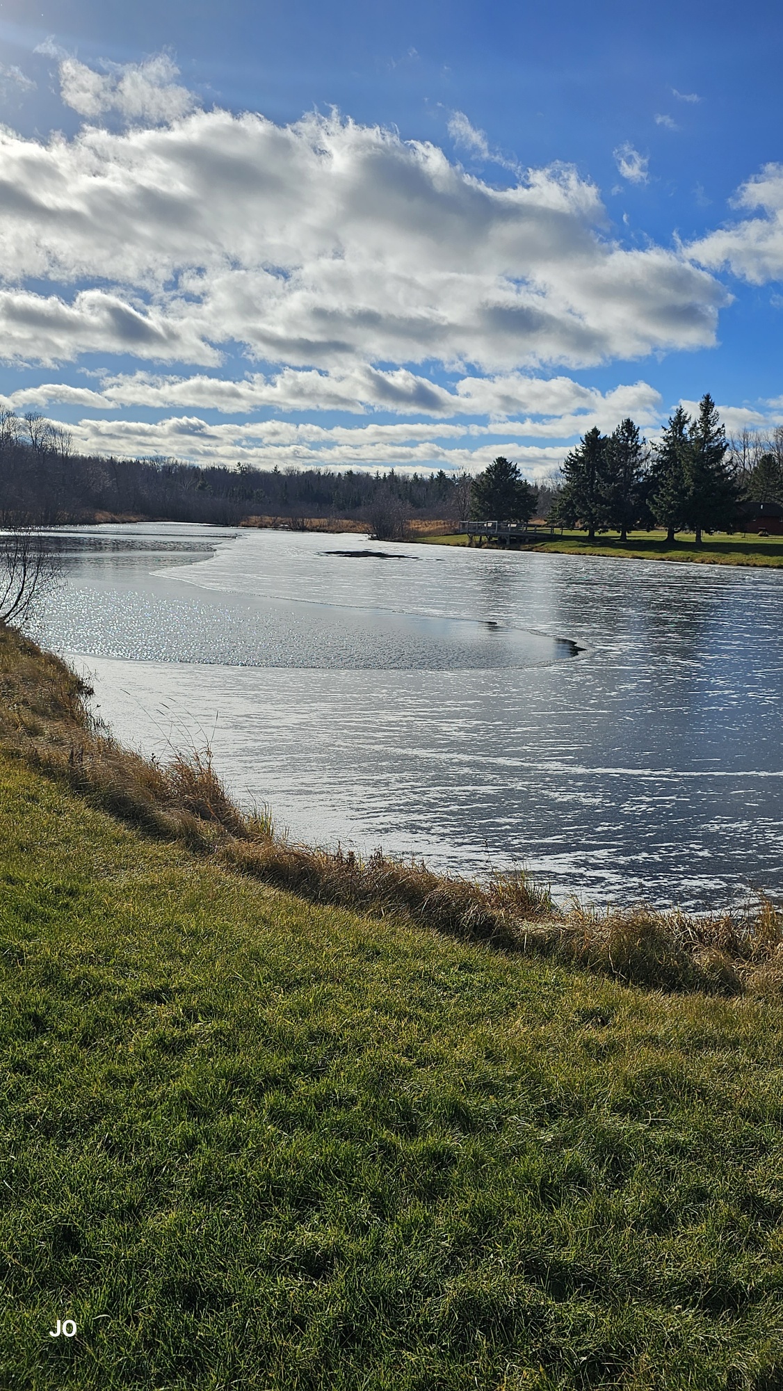 Sunny day over partially frozen pond with clouds.