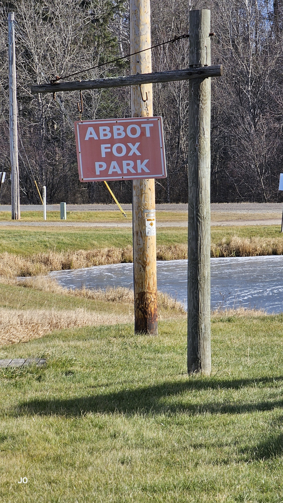Abbot Fox Park sign on wooden pole with grassy field.
