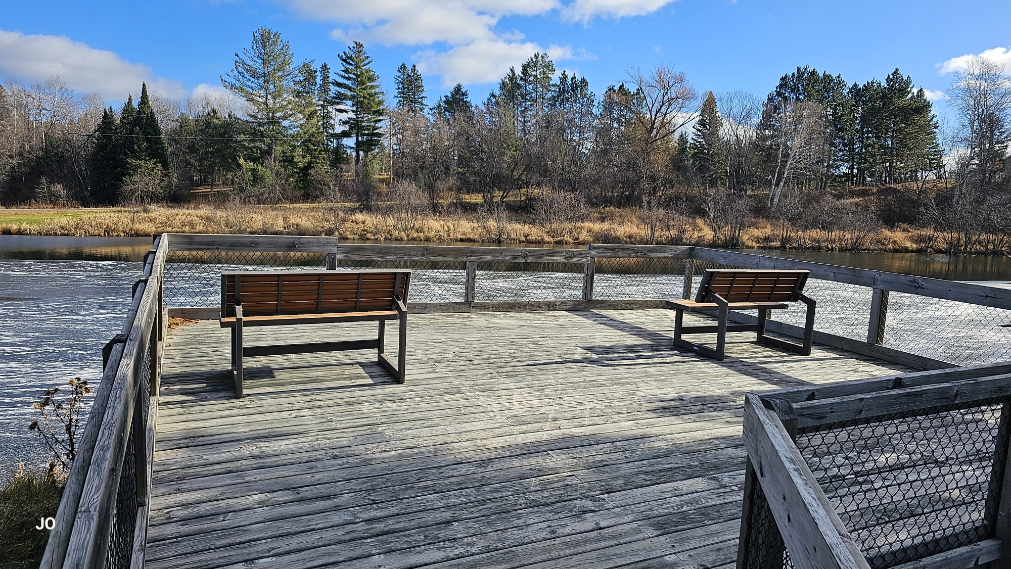 Wooden pier with benches overlooking serene river landscape.