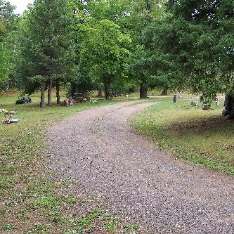 Curving gravel path through peaceful cemetery with trees.